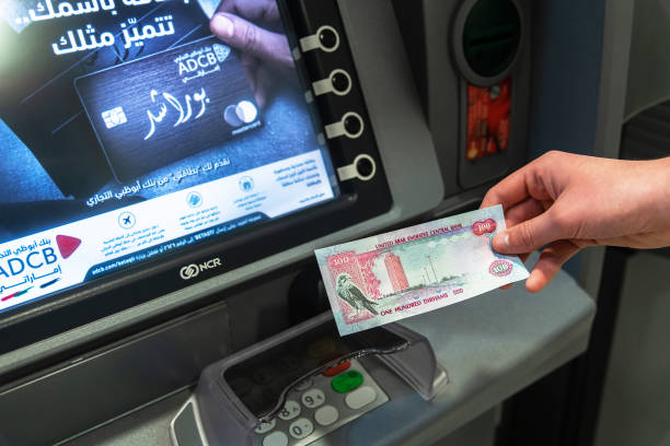 Abu Dhabi, UAE - March 29. 2019. 100 dirham in hand against background ATM of Abu Dhabi Commercial Bank stock photo