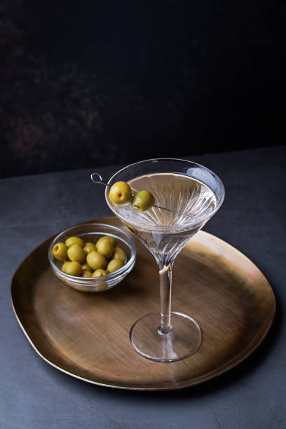 Dirty martini cocktail in martini glass with olives garnish on dark table Dirty martini cocktail in back light with olives garnish on dark stone table, top view, copy space dirty martini stock pictures, royalty-free photos & images