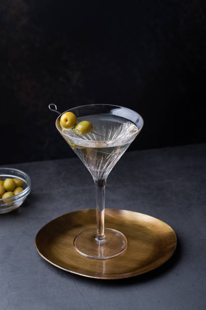 Dirty martini cocktail in martini glass with olives garnish on dark table Dirty martini cocktail in back light with olives garnish on dark stone table, top view, copy space dirty martini stock pictures, royalty-free photos & images