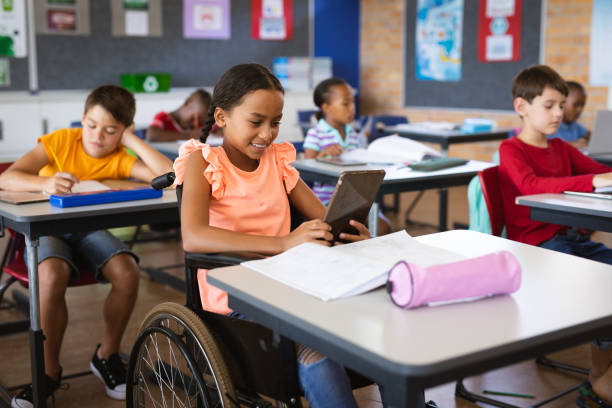 Disabled african american girl using digital tablet while sitting on wheelchair at elementary school stock photo