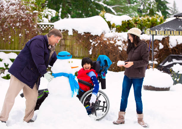 Disabled boy in wheelchair building snowman with family during  winter stock photo