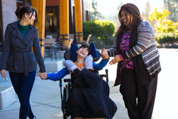 Disabled boy in wheelchair holding hands with caregivers on walk stock photo