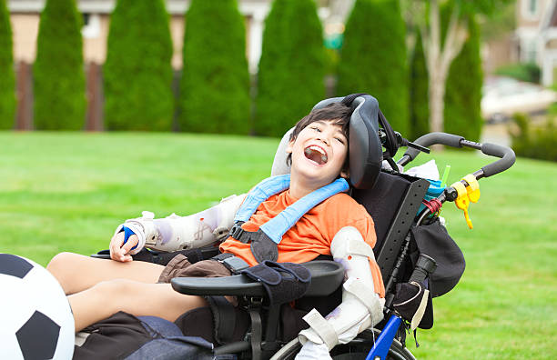 Disabled boy in wheelchair playing with soccer ball at park stock photo