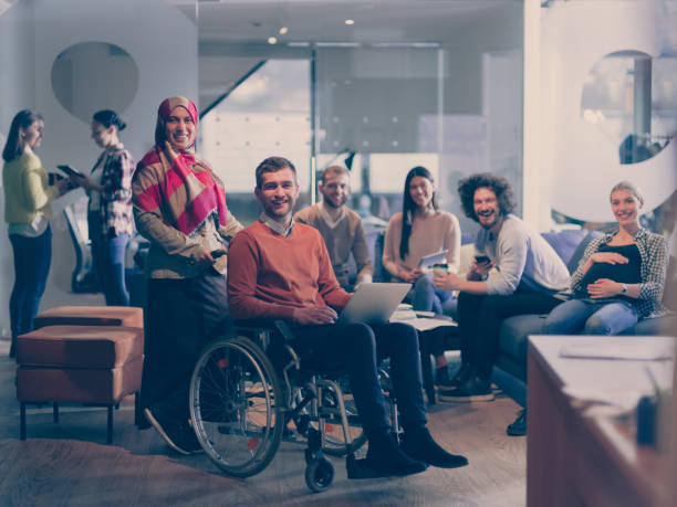 Disabled businessman in a wheelchair at work in modern open space coworking office with team stock photo