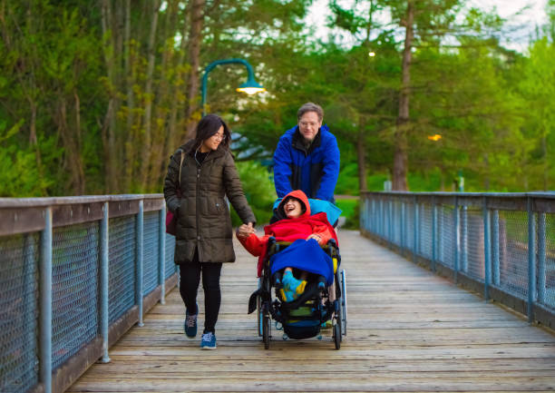 Disabled child in wheelchair at park with father and sister stock photo