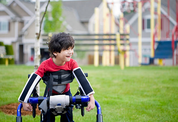 Disabled four year old boy standing in walker by playground stock photo