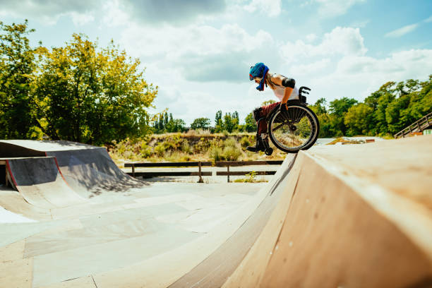 Disabled millennial woman in wheelchair rolls down the hills in skate park Wheelchair woman performing stunts in skate park - courage and confidence in adaptive sports and hobbies wheelchair stock pictures, royalty-free photos & images
