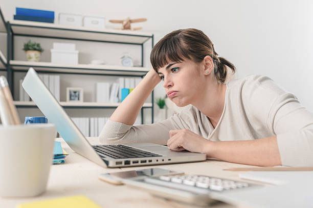 Disappointed woman working with a laptop Tired disappointed woman working at office desk with a laptop, connection and computer problems concept boredom stock pictures, royalty-free photos & images