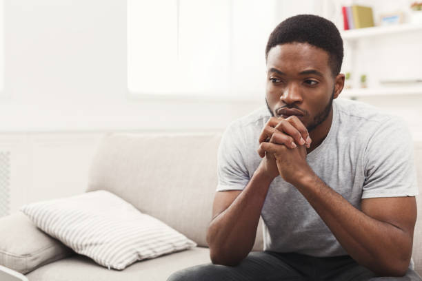 Disappointed young african-american man at home Young african-american man sitting at home. Sad guy sitting on the couch , copy space disappointment stock pictures, royalty-free photos & images