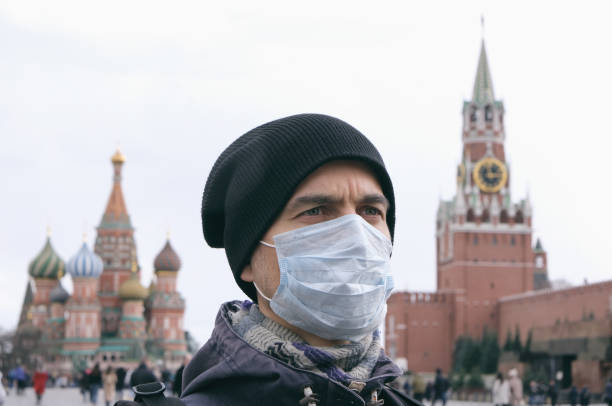 질병 발발, 코로나 바이러스 covid-19 전염병, 모스크바, 러시아에서 대기 오염. 배경에 크렘린과 붉은 사각형과 얼굴에 의료 보호 마스크와 성인 남자의 초상화. - 러시아 뉴스 사진 이미지