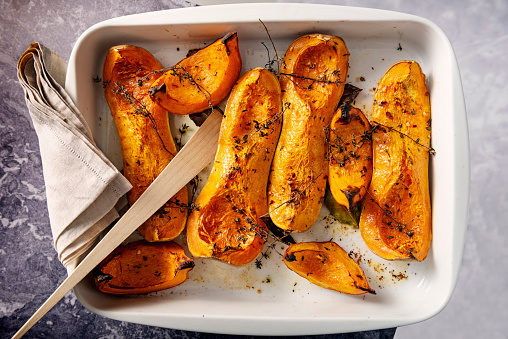 Dish of freshly roasted Butternut squashes cooked until they are soft, with thyme, bay leaves and olive oil. Colour, horizontal with some copy space.