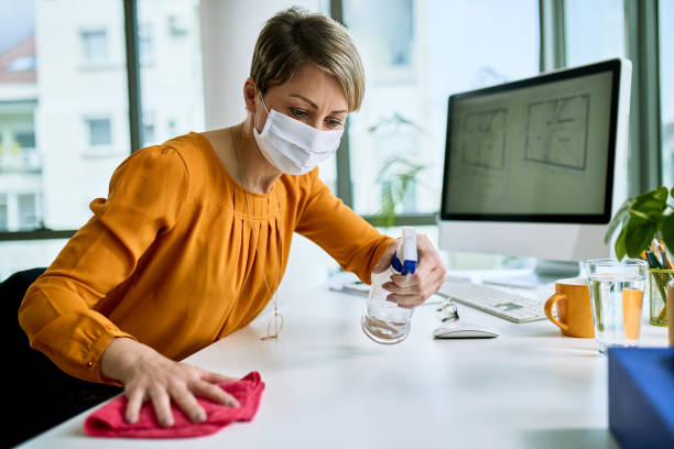 Disinfecting her workspace! Businesswoman with face mask disinfecting her desk while working in the office during virus epidemic. clean desk stock pictures, royalty-free photos & images