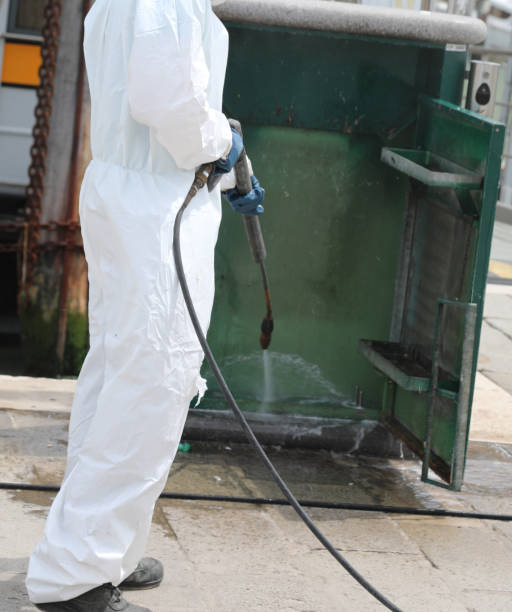 disinfestation with a pressure washer of street furniture during the coronavirus epidemic with the worker in protective suit stock photo