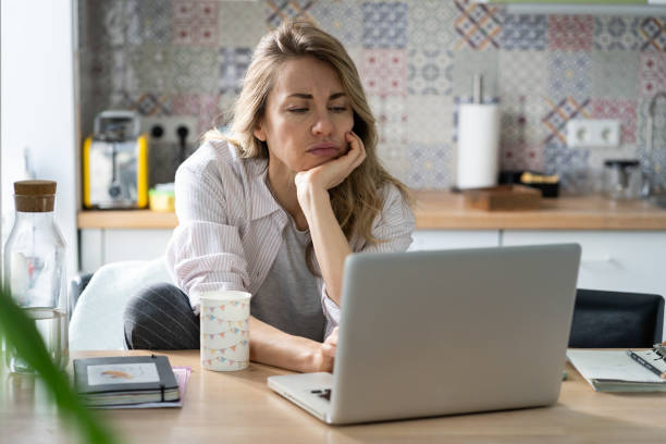 Displeased woman of middle age search for new job unemployed during covid-19 quarantine on laptop stock photo