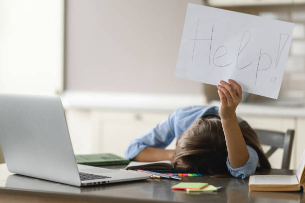 Distance learning. The schoolgirl is tired of studying. A frustrated caucasian schoolgirl, tired of studying at home, lies at her desk and holds a leaflet with the inscription help stock photo
