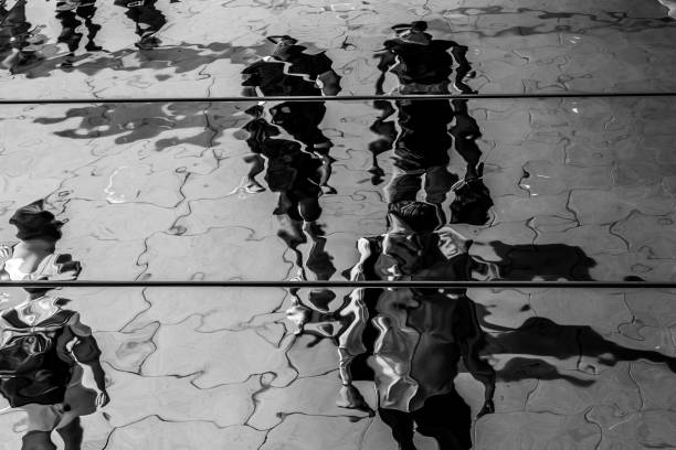 Distorted reflection and shadow of pedestrians on the ceiling of a canopy The distorted reflection and shadows of pedestrians walking on a public sidewalk.  The reflection is cast by a metallic canopy that stretches across the sidewalk.  London, England. Monochrome. distorted stock pictures, royalty-free photos & images