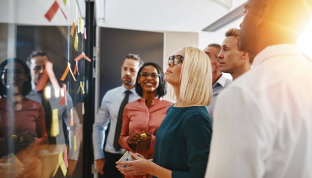 Diverse businesspeople standing in an office brainstorming with sticky notes stock photo