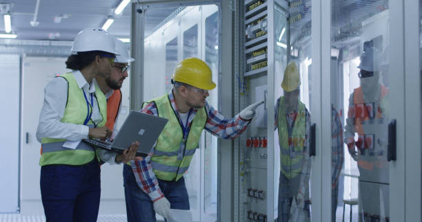 Diverse engineers with papers working in control center between racks Group of multiethnic men and woman in hardhats working in hall of solar plant control center having discussion between racks power supply stock pictures, royalty-free photos & images