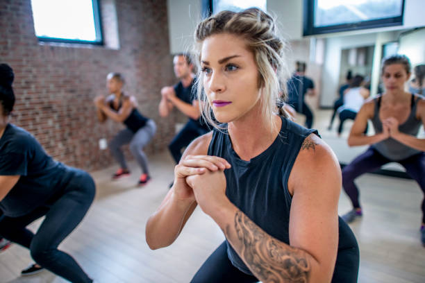 Diverse fitness class doing squats Diverse group of young adults doing squats in unison during a fitness class 30 39 years stock pictures, royalty-free photos & images