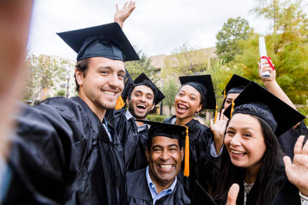 Diverse friends group takes joyful photo after graduation The diverse group of friends takes a selfie as they smile and cheer after the graduation ceremony. public universities in usa stock pictures, royalty-free photos & images