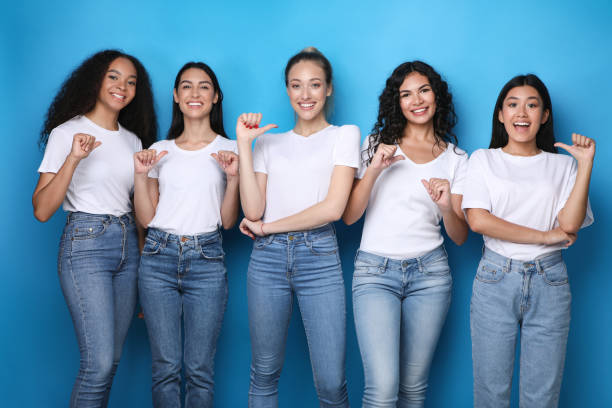 Diverse Girls Pointing At Themselves Smiling Posing In Studio Choose Me. Diverse Girls Pointing At Themselves Smiling To Camera Posing In Studio Over Blue Background. chinese girl hairstyle stock pictures, royalty-free photos & images