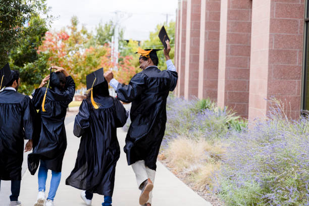 Diverse graduates walk out to family after ceremony The four multi-ethnic graduates walk out of the auditorium to meet their families after the graduation ceremony.  They are glad to be done. public universities in usa stock pictures, royalty-free photos & images