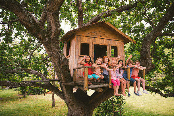Diverse group of children smiling and waving in a treehouse stock photo