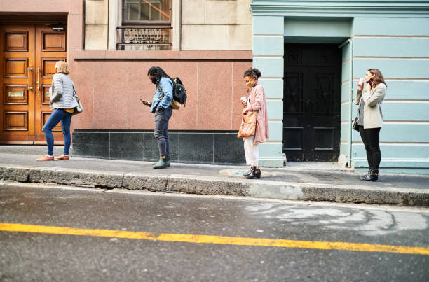 Diverse group of people in face masks social distancing on a city sidewalk Group of diverse young people wearing protective face masks practicing social distancing in a line on a city sidewalk south africa covid stock pictures, royalty-free photos & images