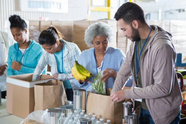 Diverse group of volunteers in food bank Happy group of people work together in food bank. They are sorting through donated food items. food bank stock pictures, royalty-free photos & images