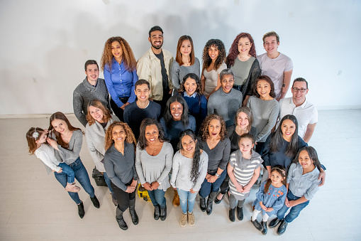 A large diverse group of people pose in a studio. The group is smiling and wearing semi-casual clothing. The image is shot from above and the group is looking up at the camera.