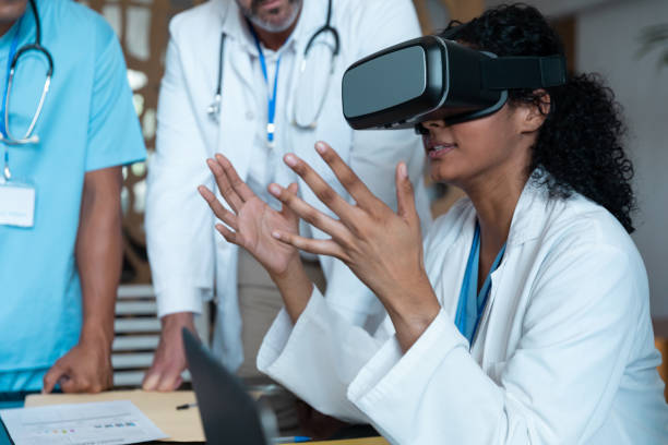 Diverse male and female doctors wearing face masks sitting at table and using vr glasses stock photo
