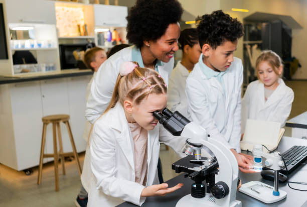 Diverse schoolchildren with teacher work together on science project, using microscope stock photo