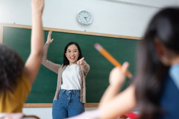 Diverse Student raising their hands up in classroom at international elementary school. stock photo