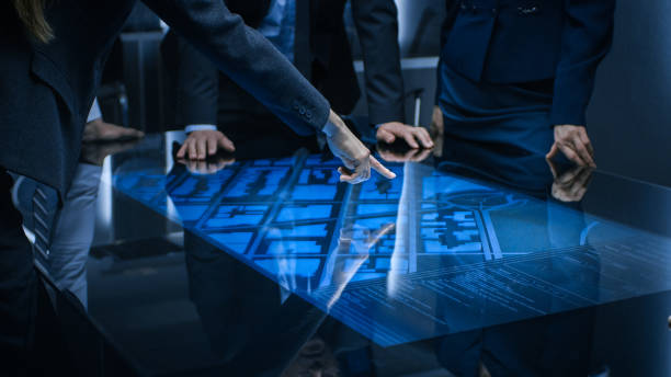 Diverse Team of Government Intelligence Agents Standing Around Digital Touch Screen Table and Satellite Tracking Suspect, Pointing at Display. Big Dark Surveillance Room. Diverse Team of Government Intelligence Agents Standing Around Digital Touch Screen Table and Satellite Tracking Suspect, Pointing at Display. Big Dark Surveillance Room. touch screen stock pictures, royalty-free photos & images