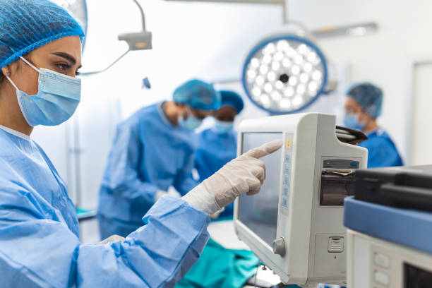 Diverse Team of Professional Surgeons Performing Invasive Surgery on a Patient in the Hospital Operating Room. Nurse Hands Out Instruments to surgeon, Anesthesiologist Monitors Vitals. stock photo