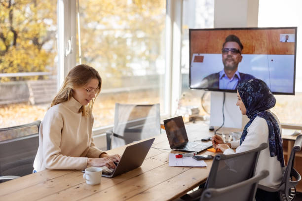 Diverse team planning in board room with a colleague on a hybrid video call stock photo