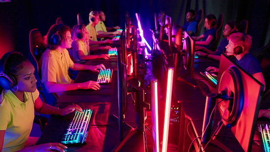 Diverse gamer group with african ethnicity players playing competitive MOBA PvP top down view computer game on a stage. Wearing headset and talking into the microphone to communicate with the yellow pro team.
