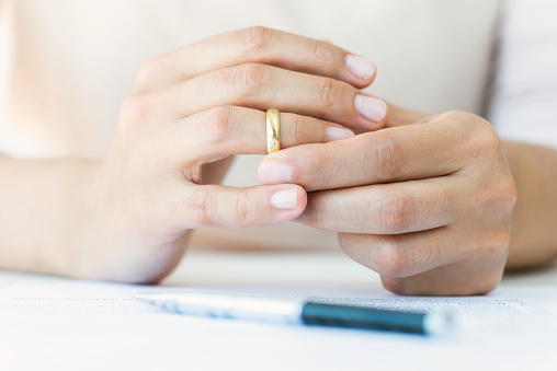 Hands of caucasian female who is about to taking off her wedding ring. Divorce papers are in front of her waiting to be signed.