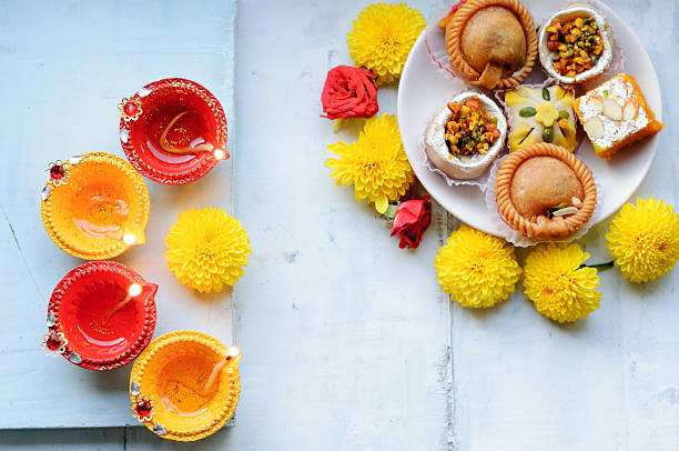 diya lamps lit during diwali celebration with flowers and sweets on a blue background  mithai stock pictures, royalty-free photos & images