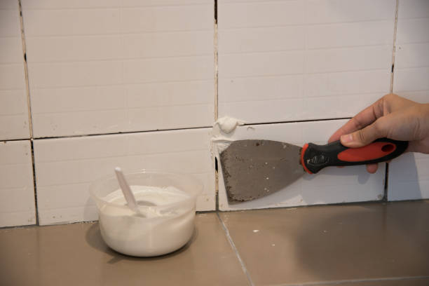DIY.The worker repairing tiler on the wall with trowel, removes the glue residues from the interstice seam and install new glue or white silicone, the technology of laying tiles and finishing. stock photo