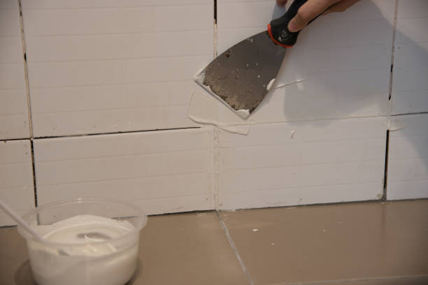 DIY.The worker repairing tiler on the wall with trowel, removes the glue residues from the interstice seam and install new glue or white silicone, the technology of laying tiles and finishing. stock photo