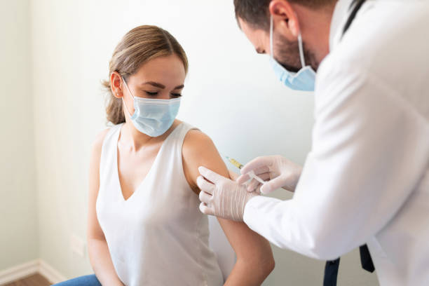 Doctor applying a vaccine on a woman's arm Closeup of a nervous woman and her doctor wearing face masks and getting a vaccine shot in a doctor's office vaccination photos stock pictures, royalty-free photos & images