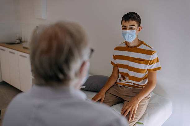 Doctor at hospital wearing mask taking care of young patient stock photo