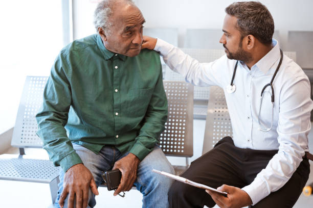 Doctor consoling sad senior male patient Healthcare worker giving bad news with hand on shoulder of male patient. Doctor consoling sad senior man in waiting room. They are sitting at hospital. sad old black man stock pictures, royalty-free photos & images