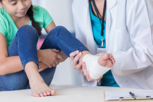 Doctor examines young girl's injured ankle Unrecognizable female doctor examines elementary age girl's injured ankle. The girl's ankle is wrapped in a white bandage. asian girls feet stock pictures, royalty-free photos & images