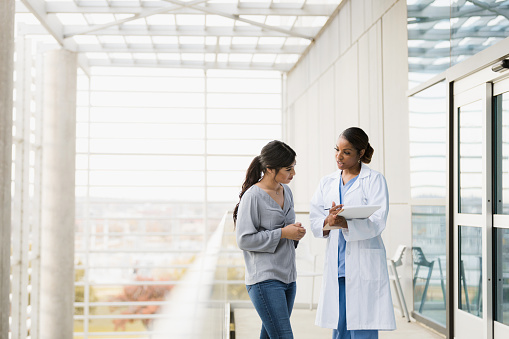 The mid adult female doctor explains the patient's test results to the young adult female family member as they stand in the hospital walkway.