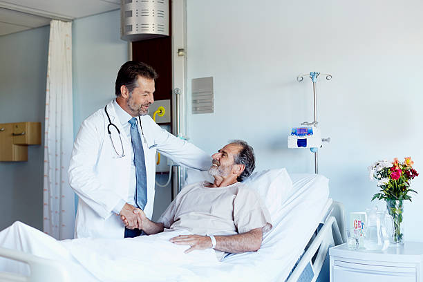 Doctor greeting patient in hospital ward Male doctor greeting patient lying in bed at hospital ward patient in hospital bed stock pictures, royalty-free photos & images