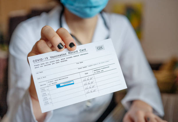 Doctor holding COVID-19 Vaccination Record Card. Close up of unrecognizable female doctor holding a COVID-19 Vaccination record card. cdc vaccine card stock pictures, royalty-free photos & images