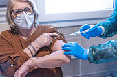 istock Doctor in hazmat suit giving patient a vaccine for coronavirus disease - Senior woman wearing protective face mask doing vaccine for Covid-19 illness - Medical and healthcare concept - Focus on gloves 1297644253
