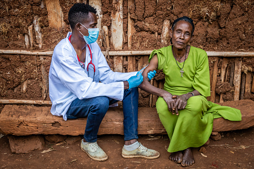Male doctor vaccinating senior African woman in small village, East Africa.